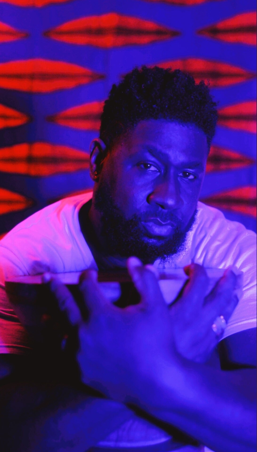 Keshida Layone in red and blue studio light, reaching toward the camera